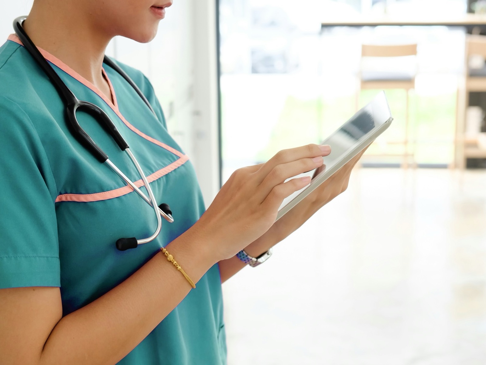 A clinician in scrubs with a stethoscope, tapping through a schedule on a tablet.